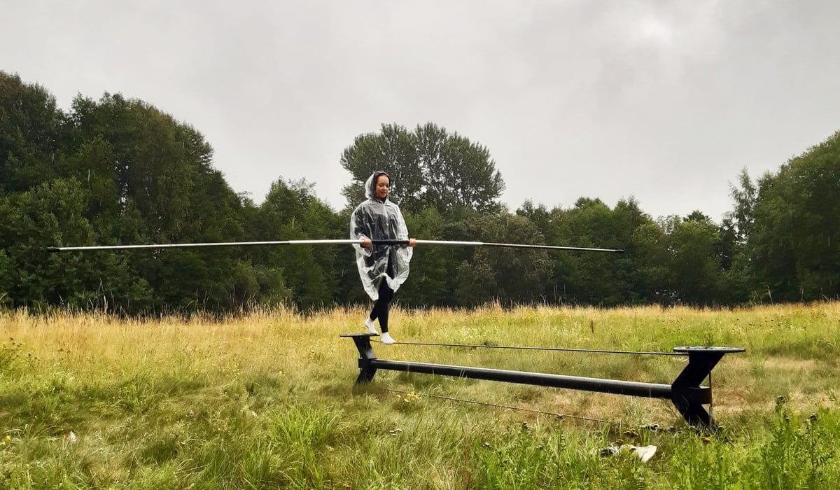 En person går på lina över ett gräsbevuxet fält med en regnponcho.