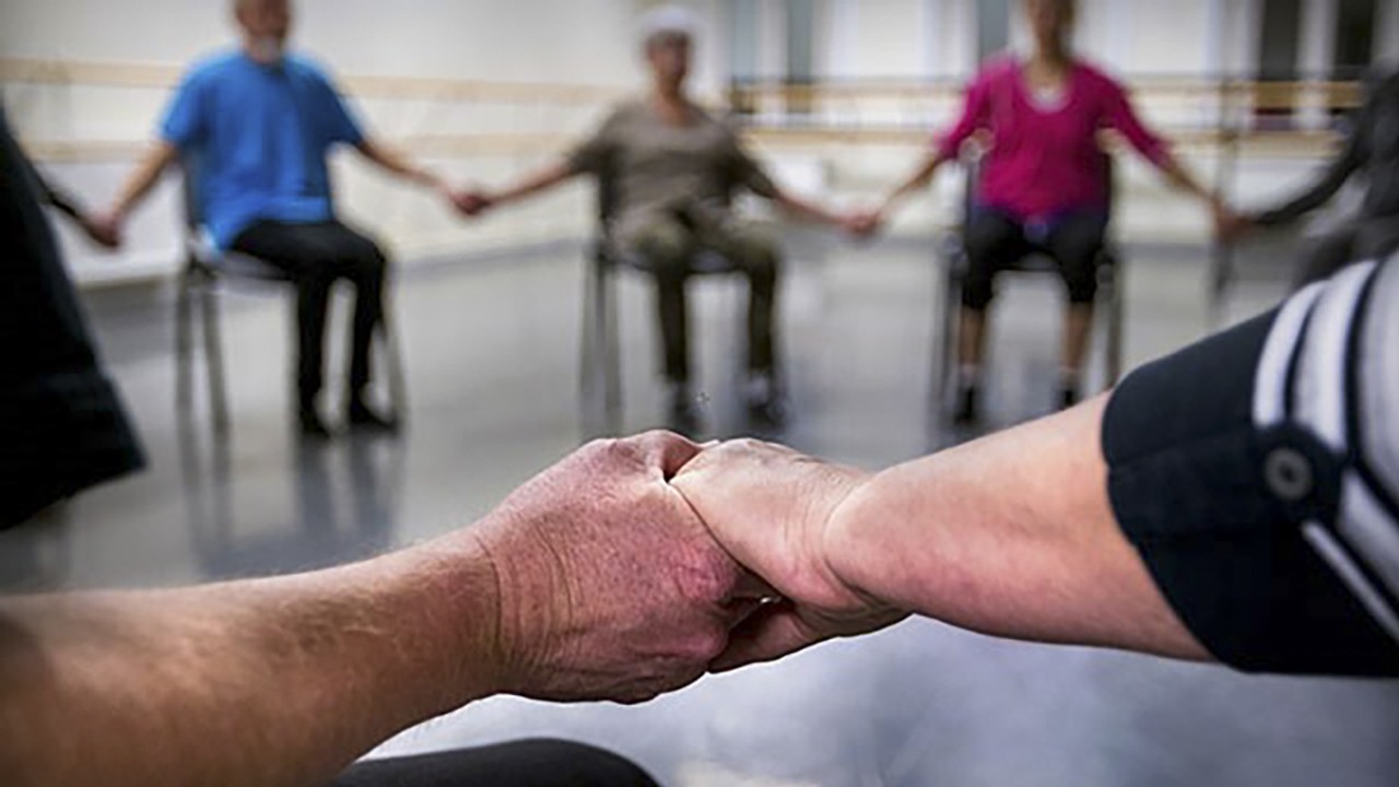 Händer som möts. Personer som sitter på stolar i en ring.