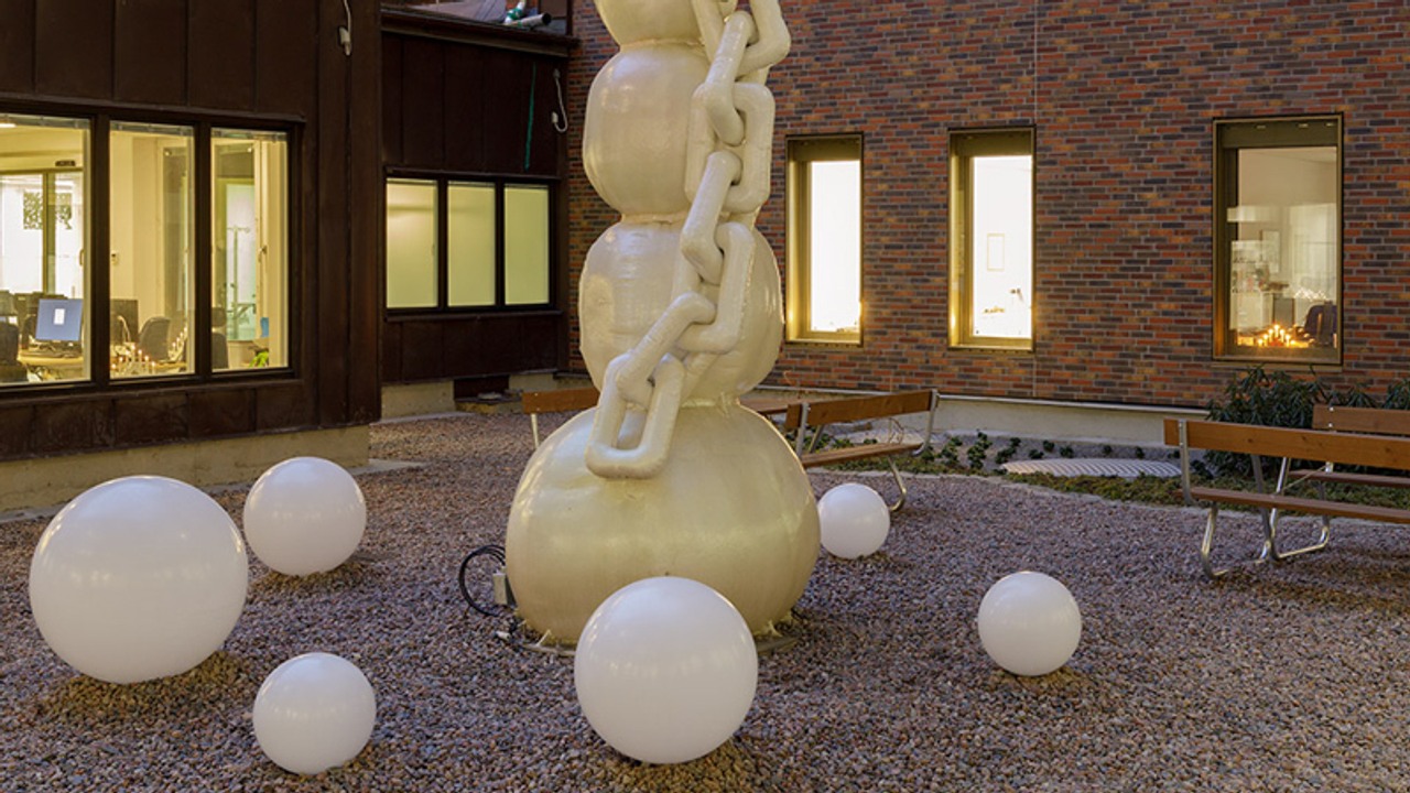 Hög skulptur på grusgård. Skulpturen är omringad av vita bollar i olika storlekar.
