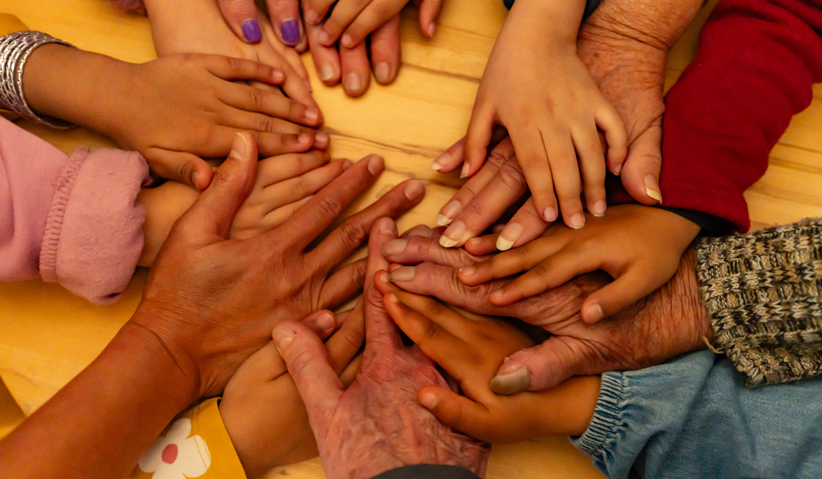 Barnhänder möter äldre personers händer i en ring ovanpå varandra