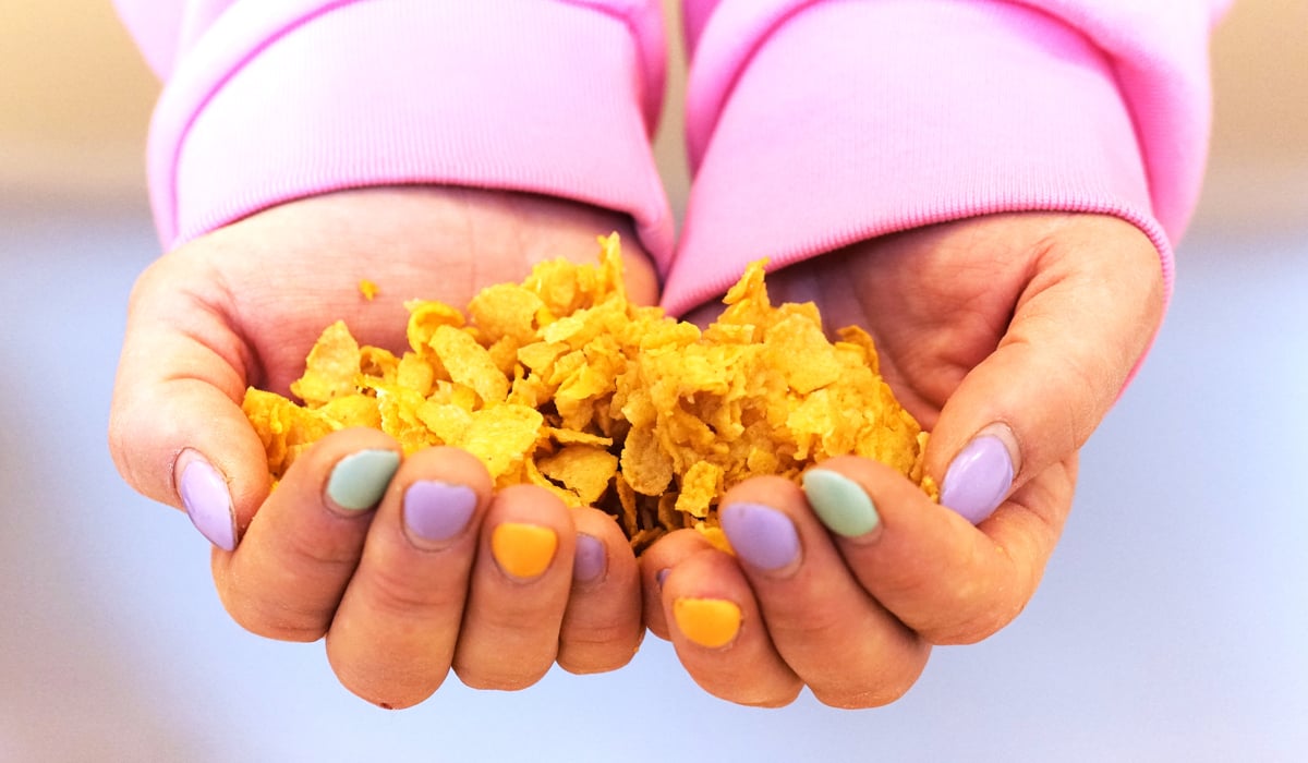 Kupade händer med målande naglar olika färger håller cornflakes.