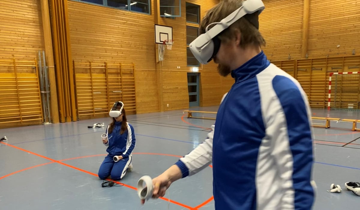 Två personer i en gymnastiksal iklädda blåa och vita träningsoveraller och vr-glasögon.