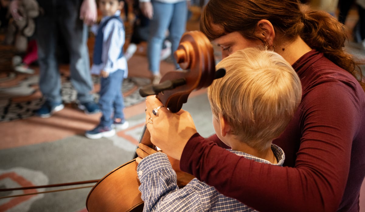 Ett barn får testa spela ett stråkinstrument med ledning av en musiker.