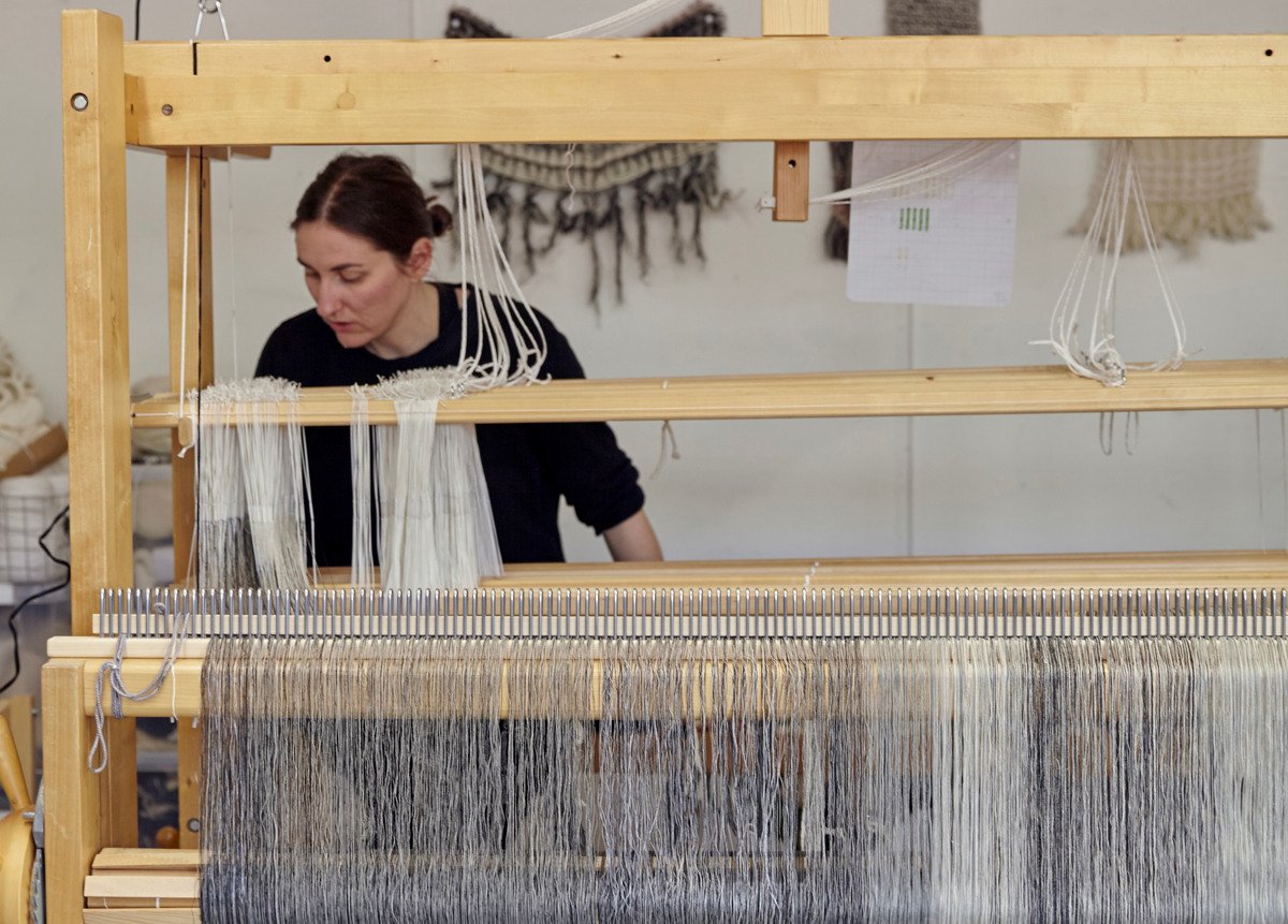 En kvinna som sitter och v&auml;ver i en v&auml;vstol.