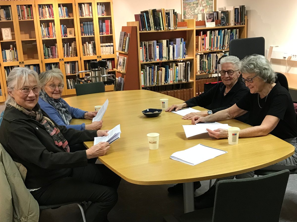 Fyra kvinnor i 70-årsåldern sitter runt ett bord inne i biblioteksmiljö.