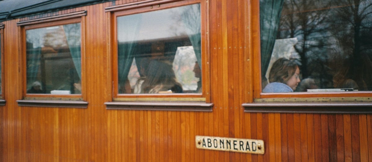 Utsida av en t&aring;gvagn i tr&auml; med m&auml;nniskor som sitter inuti den.