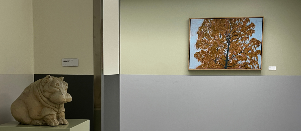 En skulptur av en flodh&auml;st som sitter p&aring; en hylla. I bakgrunden en tavla med ett tr&auml;d med bruna l&ouml;v.