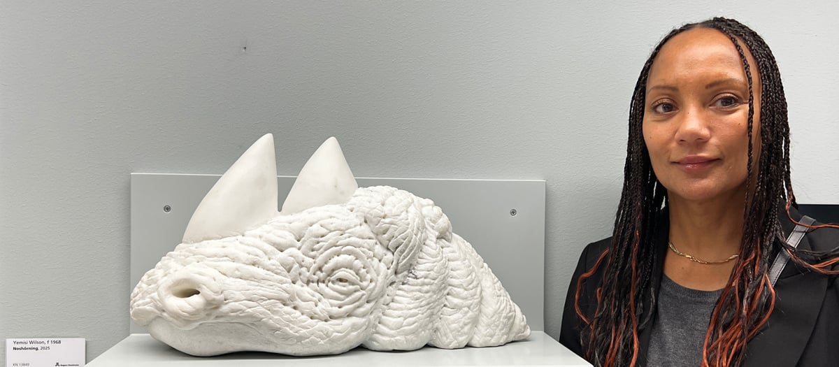 En kvinna st&aring;r bredvid en skulptur av en fisk.