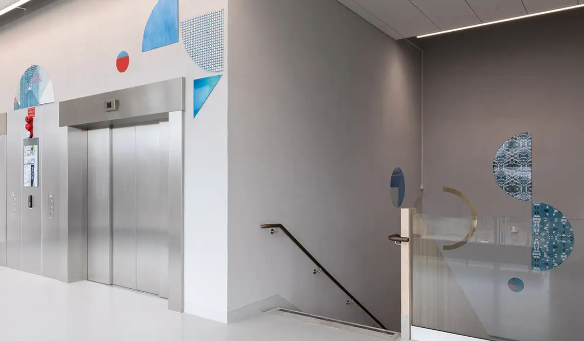 En hiss- och trapphall med konst på vägg i olika geometriska former.