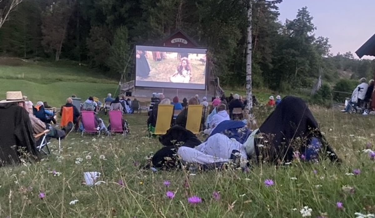 En grupp människor som sitter på ett fält och tittar på en film.