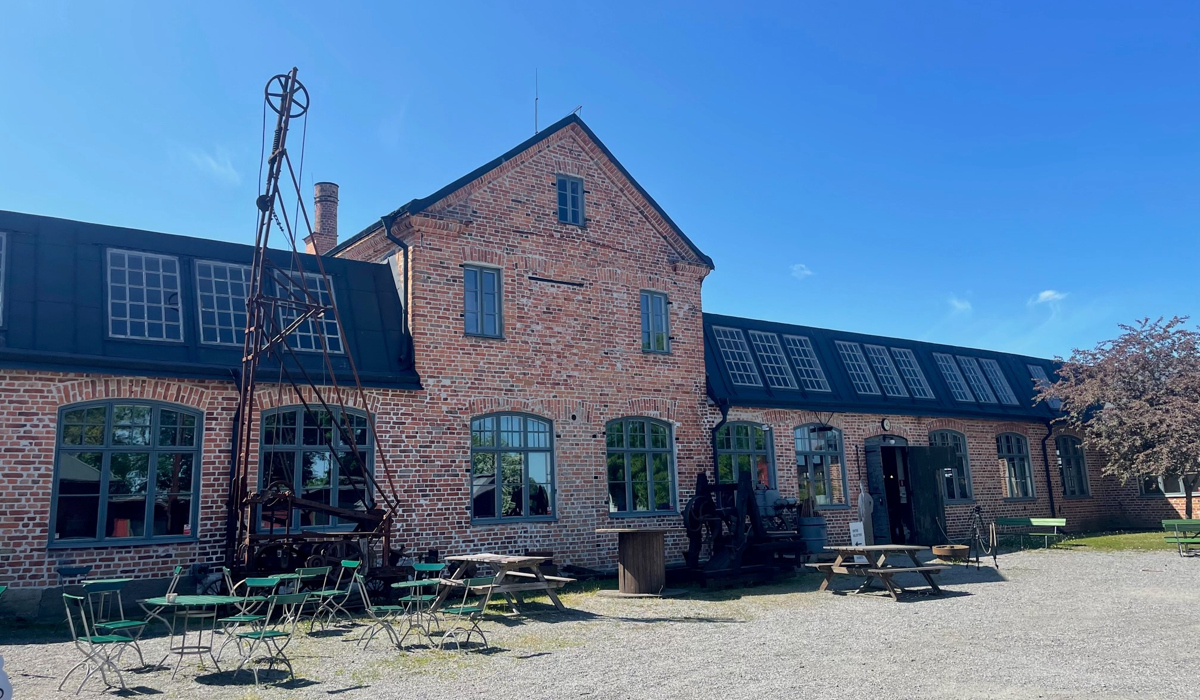 Exteriör Pythagoras industrimuseum. Röd tegelbyggnad med utemöbler framför på gårdsplan.