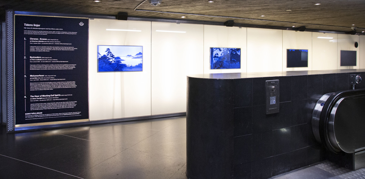 Vägg i entréhallen på Skanstull med fyra videoskärmar. I förgrunden ser man rulltrappan.