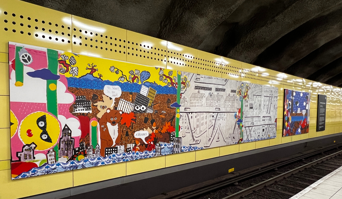 En tunnelbanestation med konsttavlor på en gul vägg.