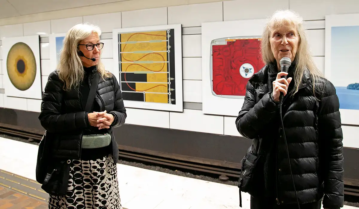 Ulla pratar i mikrofon på Gärdets tunnelbanestation. Konstguide Marie står bredvid.