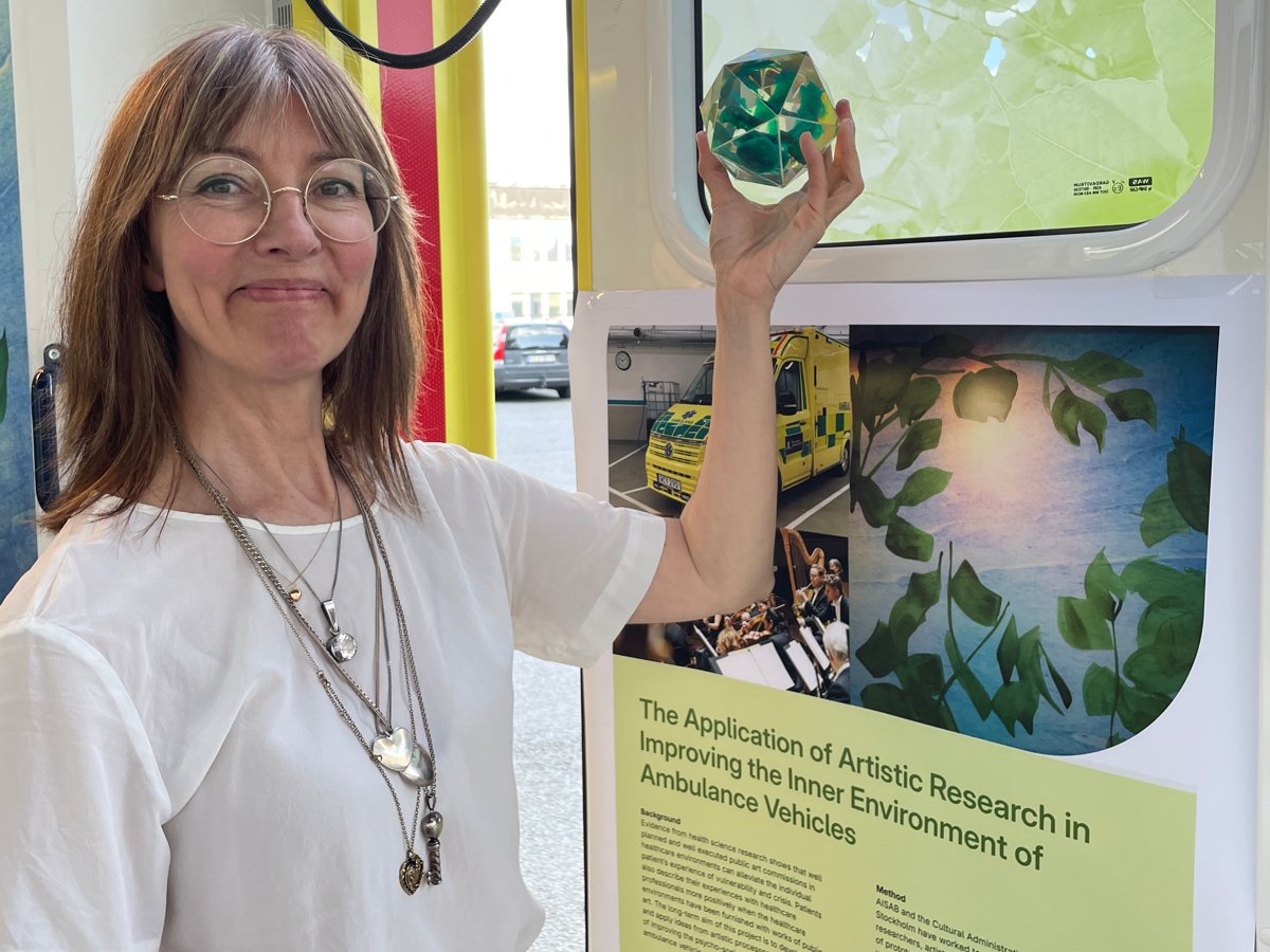 En kvinna håller upp ett grönt föremål framför en skärm.