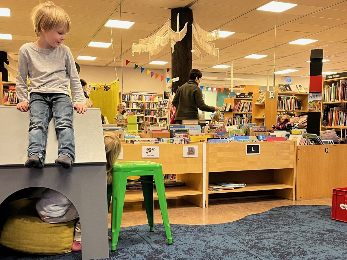 Barn sitter på lekhus i biblioteksmiljö