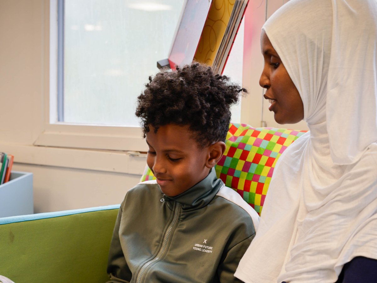 En mamma och hennes son sitter och läser en bok på bibliotek
