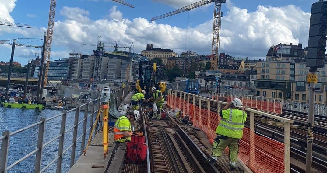 Bild på arbetare som lägger nya spår på söderströmsbron. I bakgrunden Stockholms skyline med halvmulet väder.