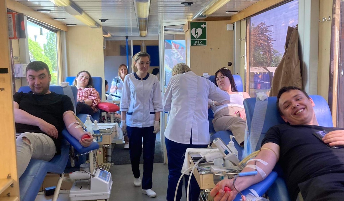 Foto inifrån blodbussen med flera personer som sitter i stolar och ger blod. Två sjuksköterskor hjälper personerna som ger blod.