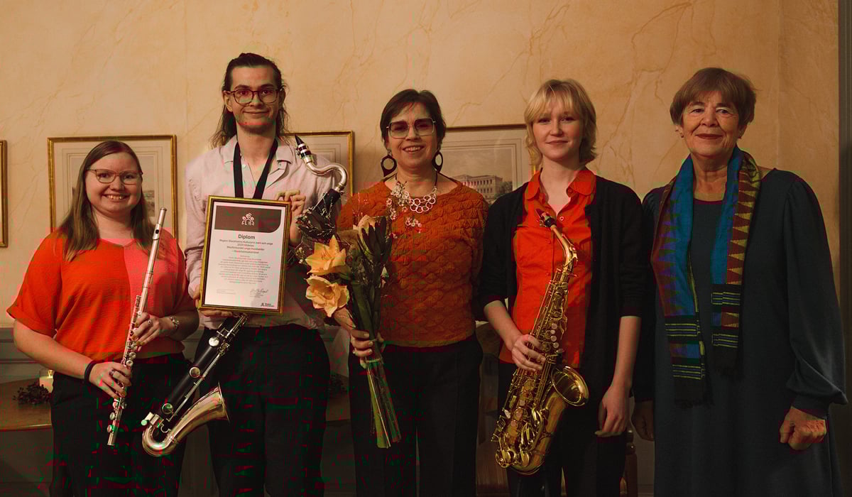En grupp personer st&aring;r bredvid varandra och h&aring;ller i diplom och musikinstrument.