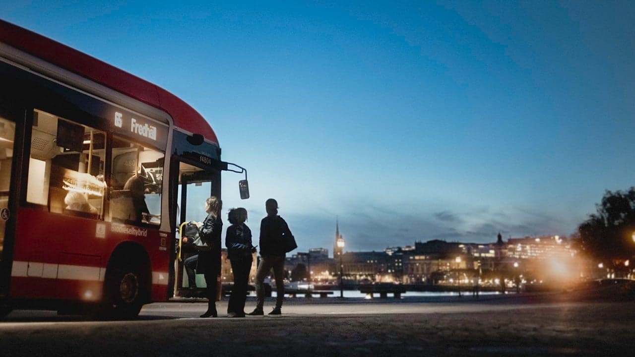 En rödbuss tar emot resenärer under skymning i Stockholm