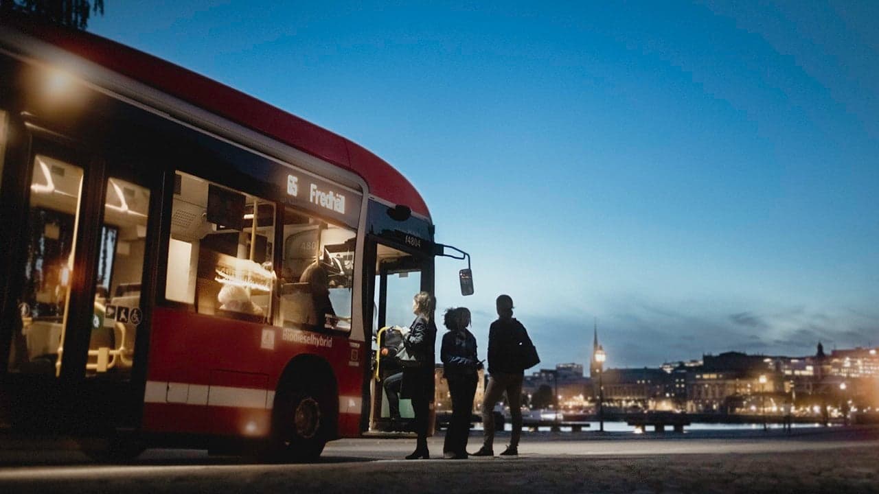 En rödbuss tar emot resenärer under skymning i Stockholm