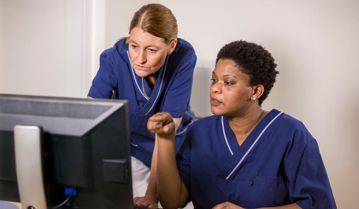 Två kollegor inom sjukvården samtalar med varandra framför en bildskärm