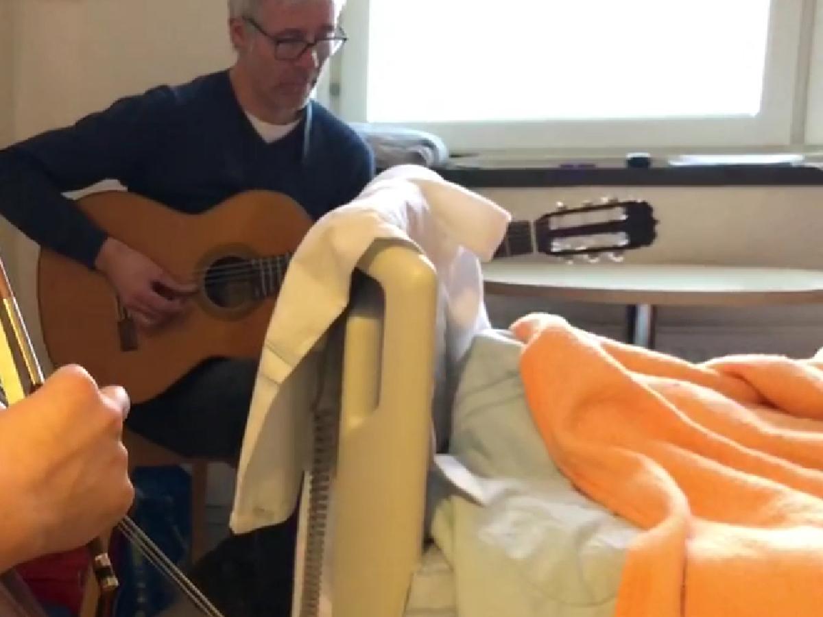 MAn spelar gitarr vid sjuksäng.