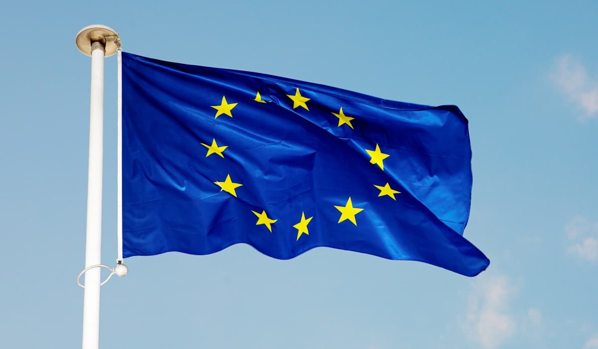 Bild på en blå EU-flagga som vajrar på en vit flaggstång med blå himmel i bakgrunden
