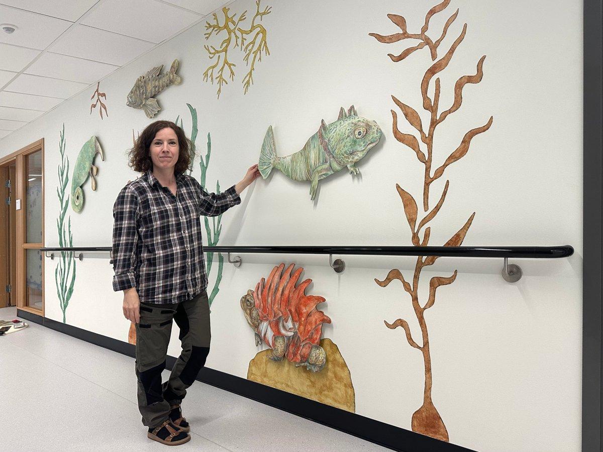 Ida håller handen mot väggen med målade växter och fantasitdjur.