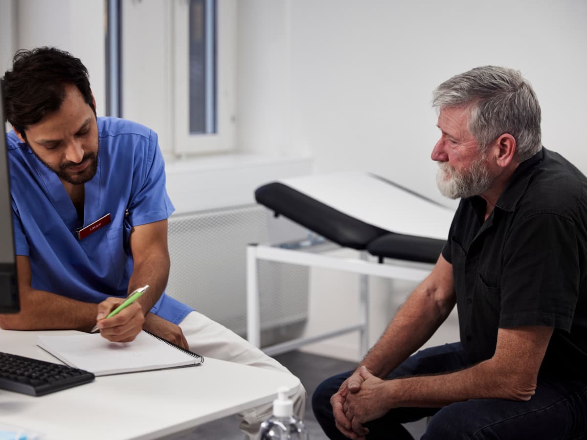 Manlig läkare ritar i ett block och talar med en manlig patient