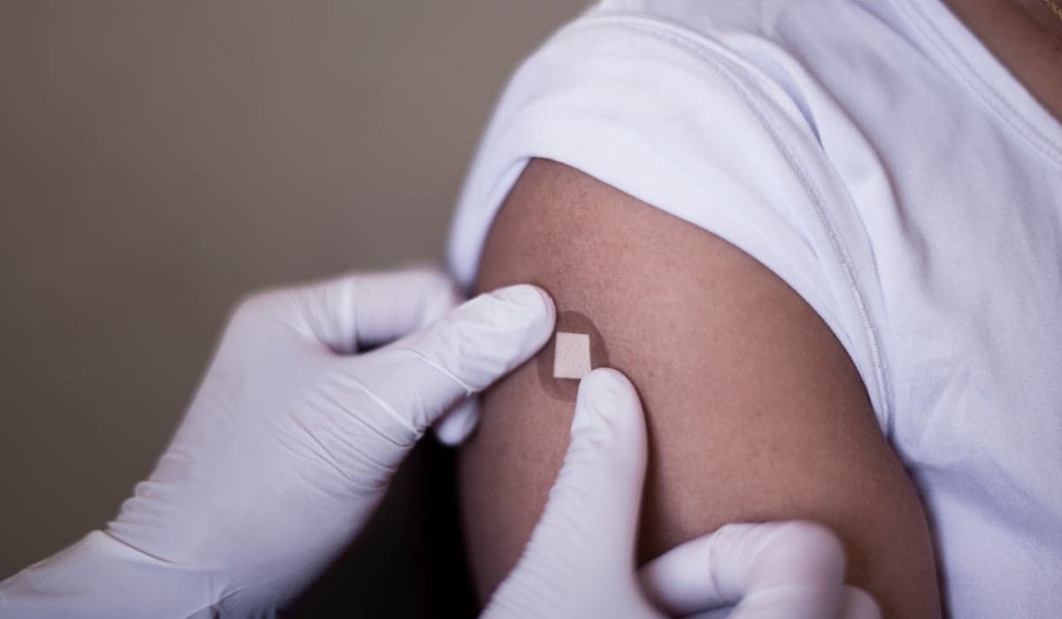 Bild på nyvaccinerad arm som precis fått en vaccinspruta. Vårdpersonal som sätter på plåster på armen.