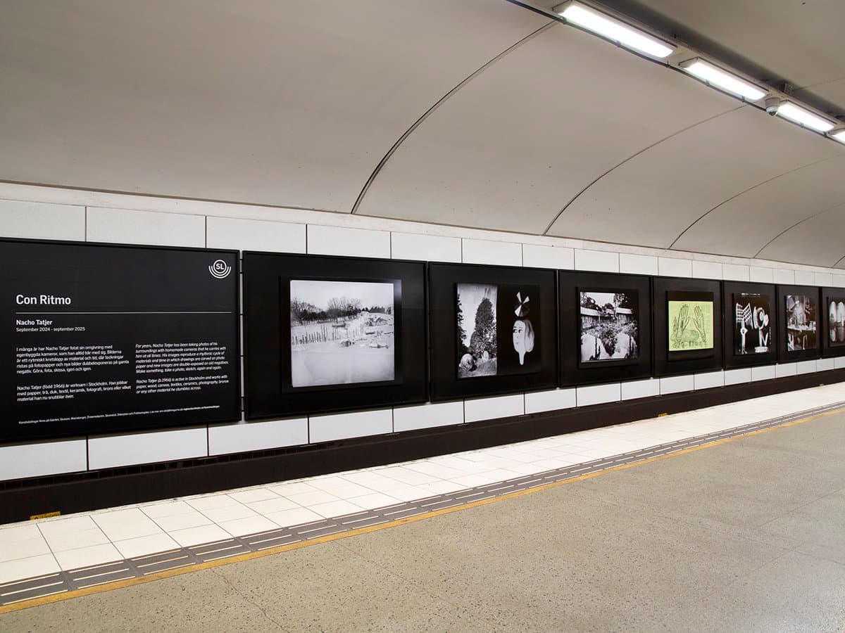 Konsttavlor på Mariatorget med svart-vita fotografier och en gul bild ritad på baksidan av en affisch.