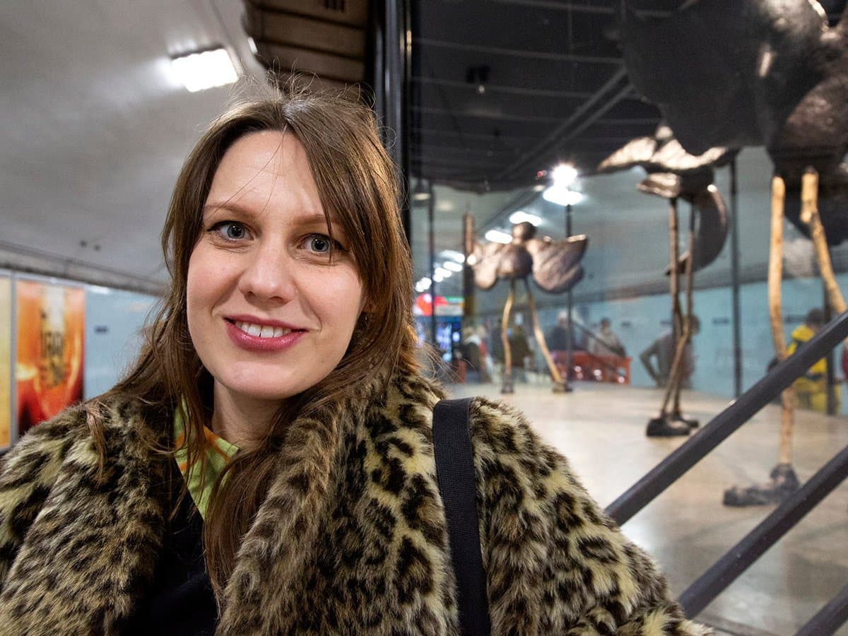 Ester på plattformen på Odenplans tunnelbanestation. Stora fågelliknande skulpturer på rad i galsmontern.
