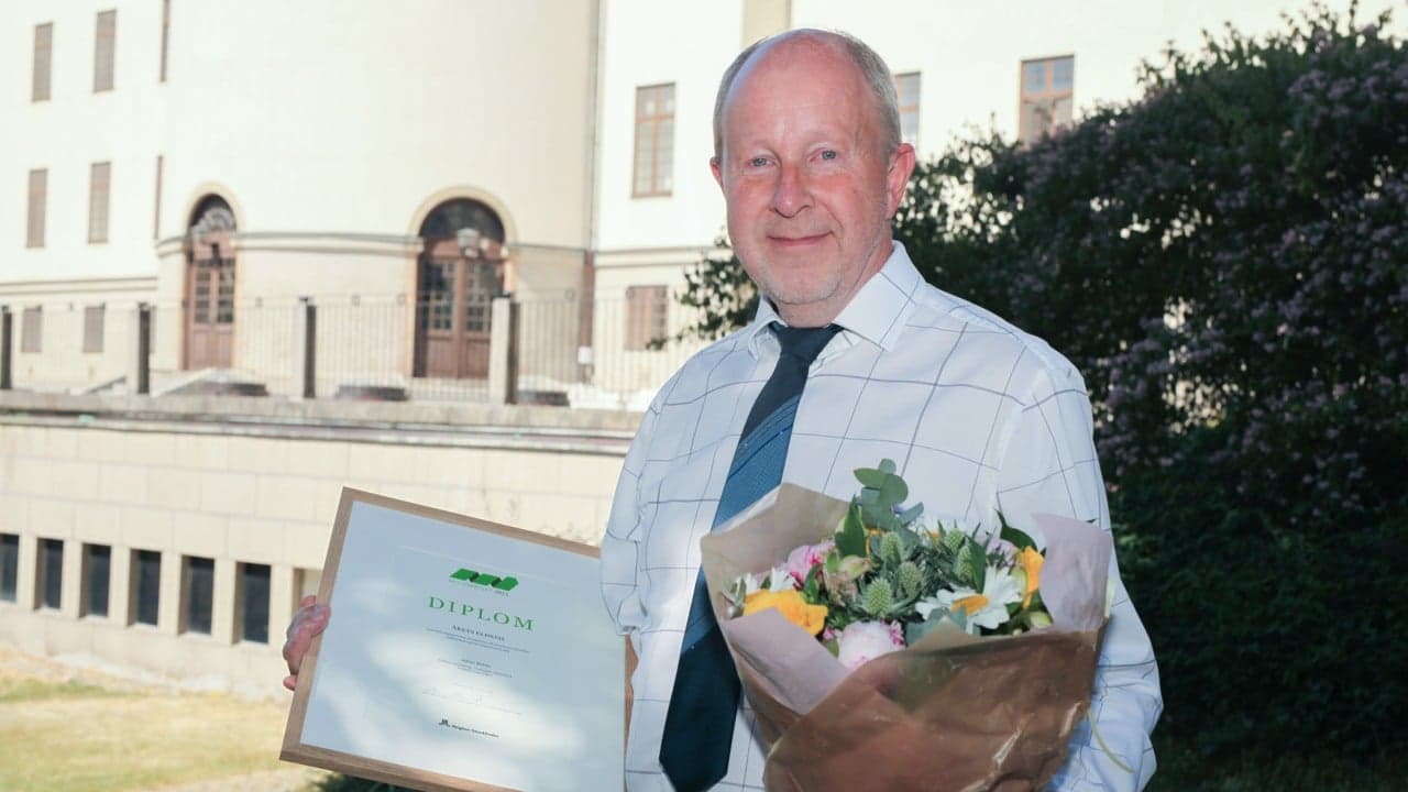 Äldre herre håller i diplom och blommor