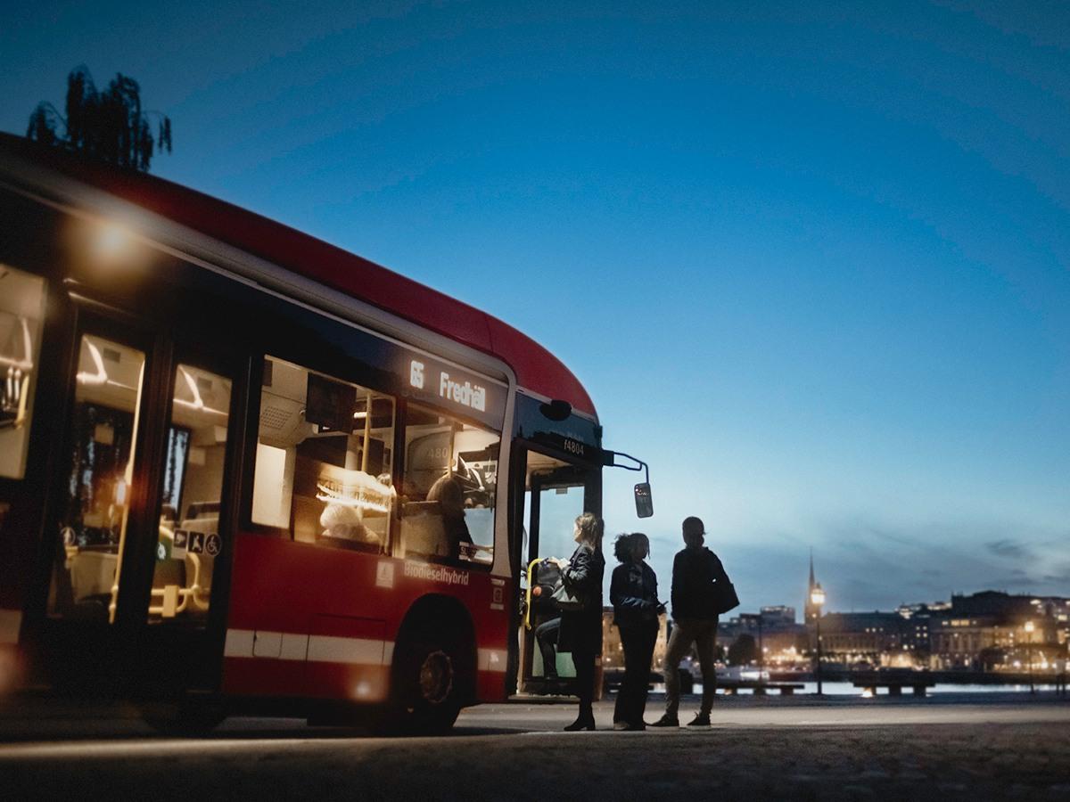 En rödbuss tar emot resenärer under skymning i Stockholm