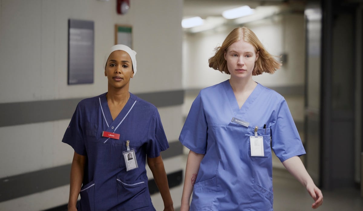 Två kvinnor i operationskläder går längs en korridor.