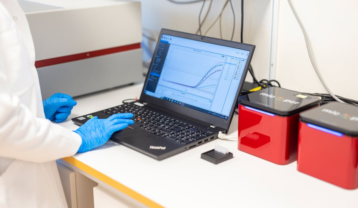 Person i labbkläder och handskar , personen läser av en kurva
 på en dataskärm