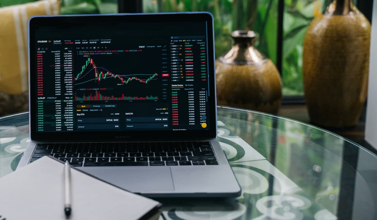 En dator som visar börsstatistik. Framför datorn finns en blädderblock och en vit penna. 
