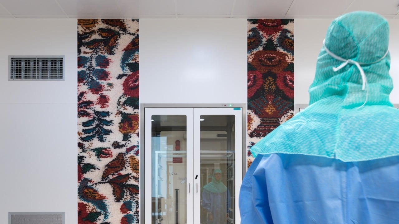 Person i skyddskläder i förgrunden. I bakgrunden vägg med två fotografier av väldigt uppförstorad textil.