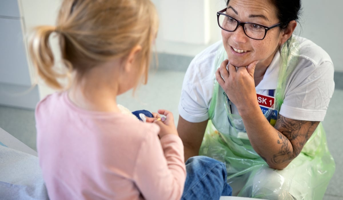 En kvinna pratar med en liten flicka som sitter på en säng.