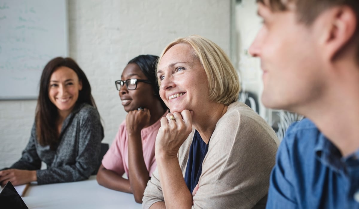 Fyra personer som sitter i ett mötesrum och lyssnar på ett möte