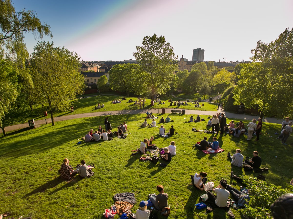 Foto på människor som sitter på filtar i en park på sommaren.
