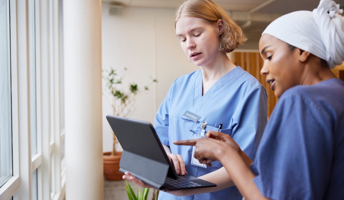 Två kvinnor i vårdkläder tittar på en bärbar dator.
