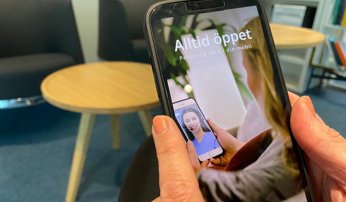 Foto på händer som håller i en mobiltelefon. På skärmen visas appen Alltid öppet