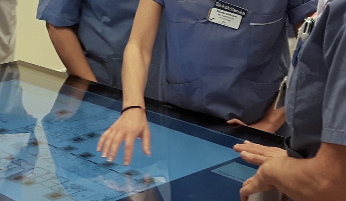 Foto på personer som står runt en liggande skärm. 