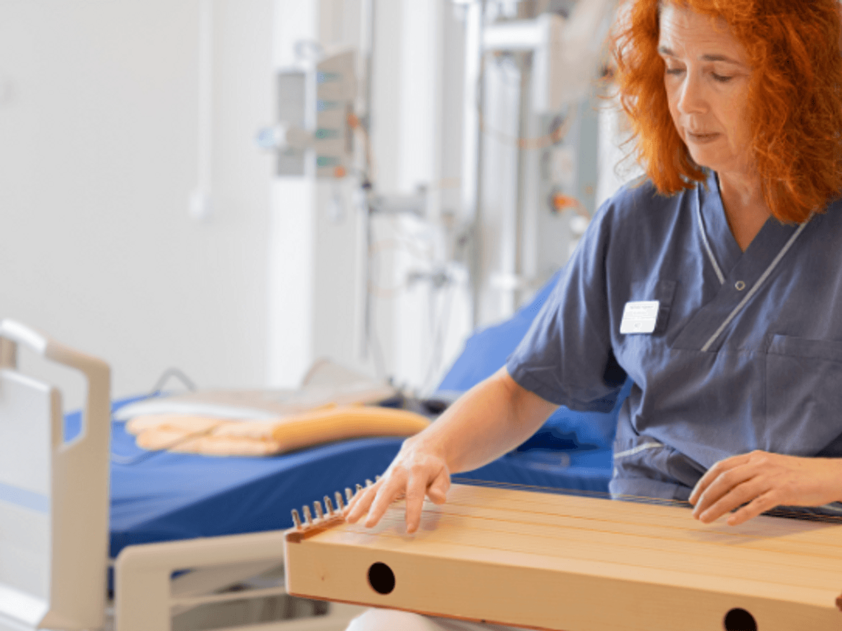 Pernilla sitter med instrument i knät. Bakom skymtar en sjukhussäng.