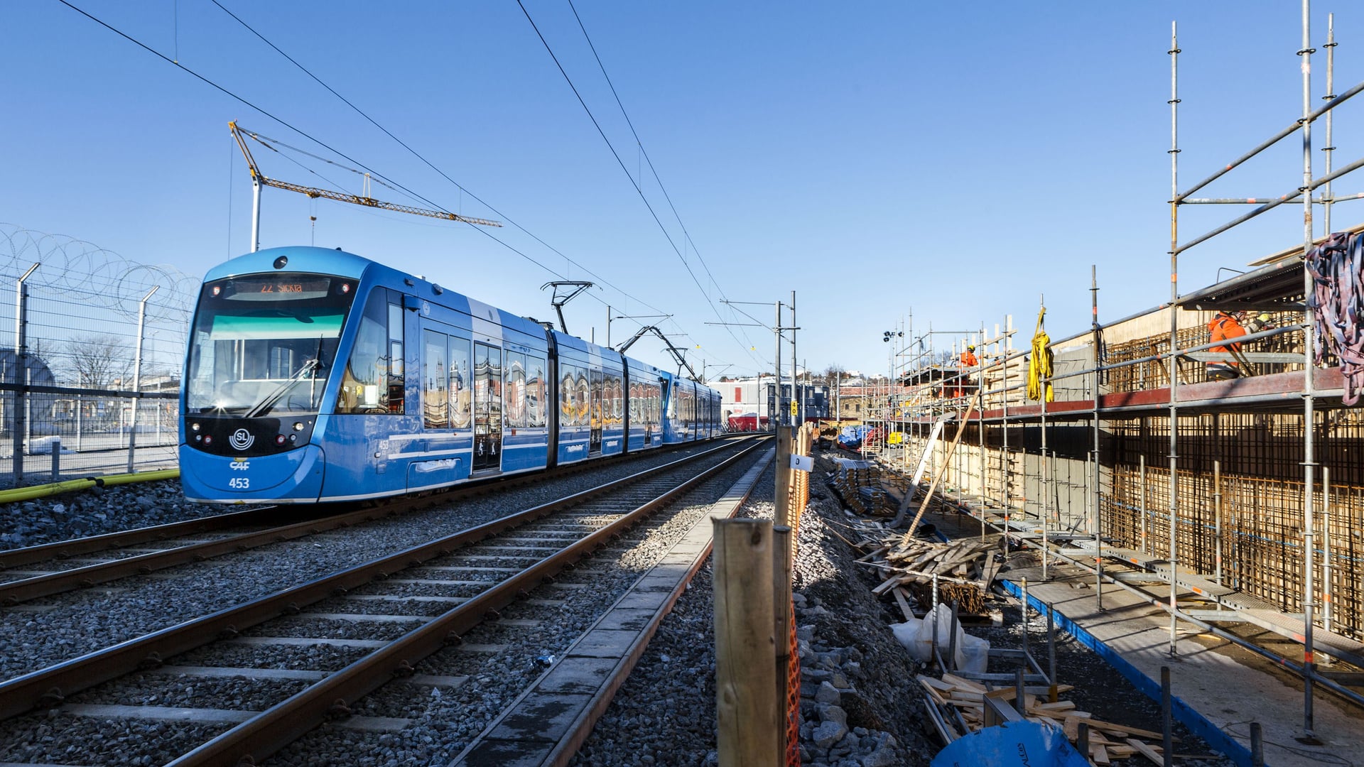 Ett blått tåg som färdas på järnvägsspår bredvid en byggnad.