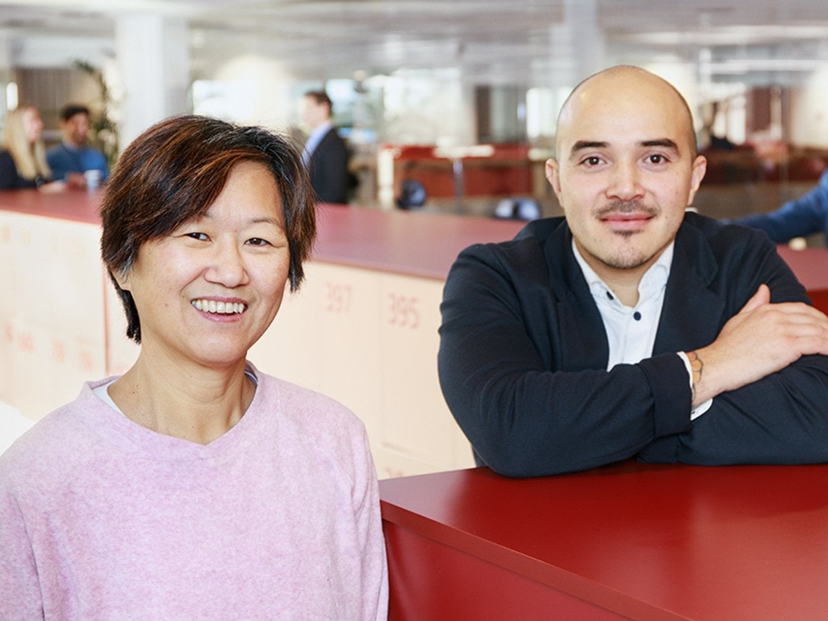 En kvinna och en  man står vid ett rött skåp i ett kontorslandskap