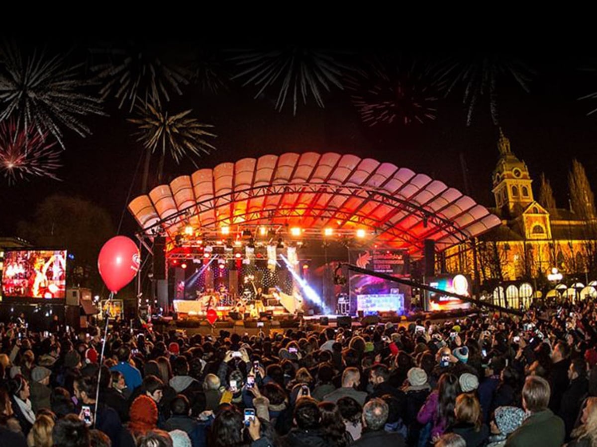 Ett publikhav framför en scen kvällstid med strålkastare och fyrverkerier.